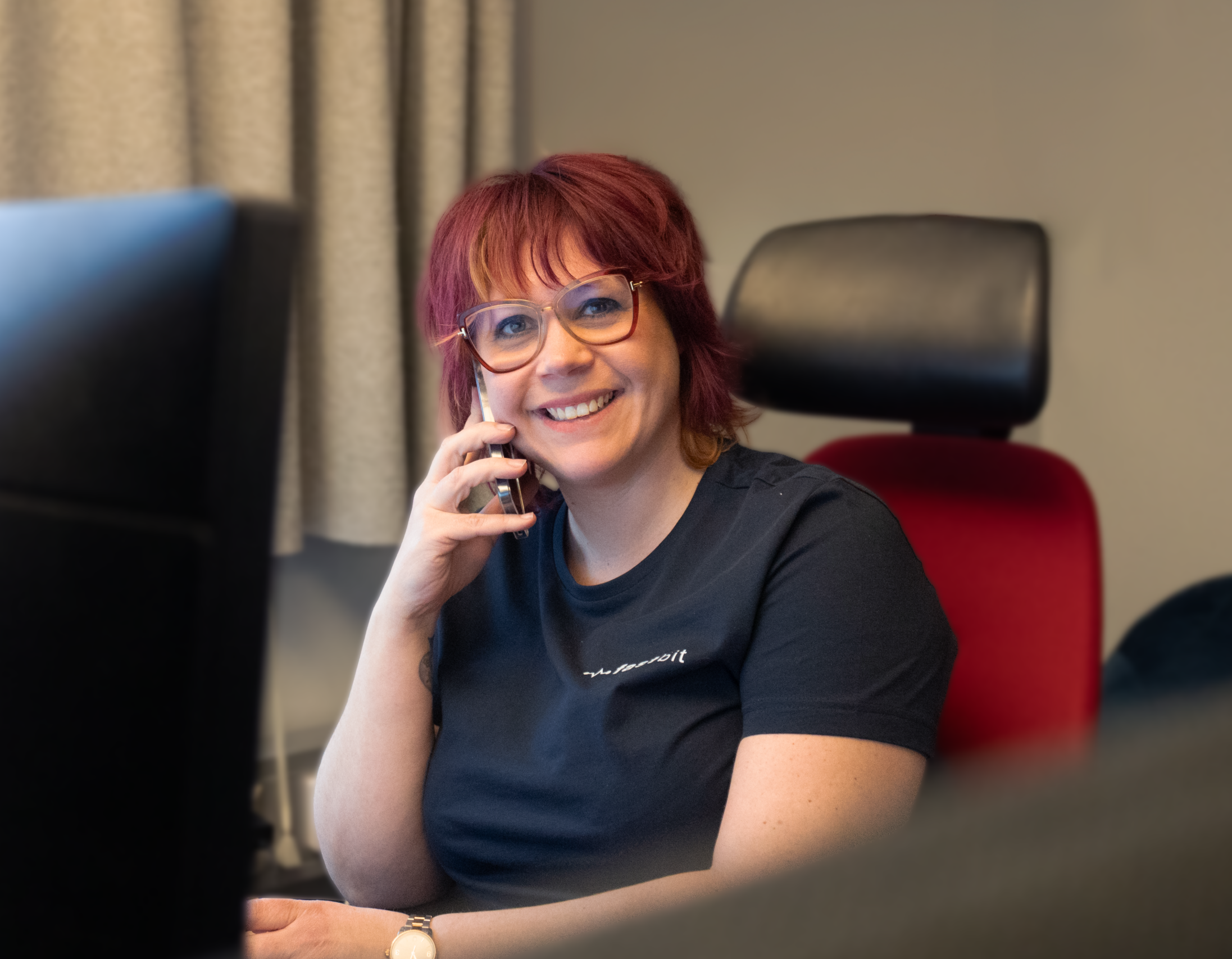 Person sitter vid ett skrivbord, håller en telefon mot örat och har en datorskärm framför sig.