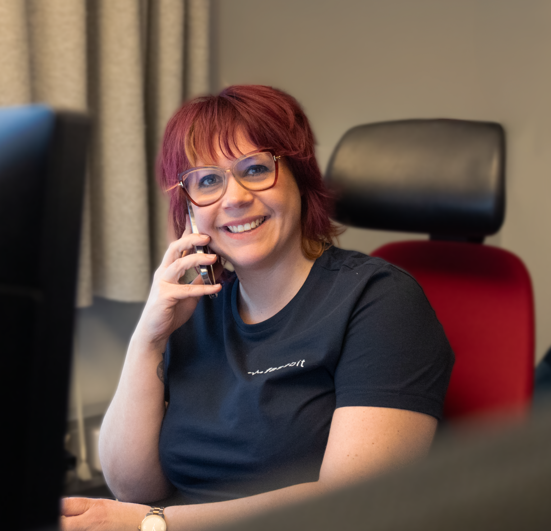 Person sitter vid ett skrivbord, håller en telefon mot örat och har en datorskärm framför sig.