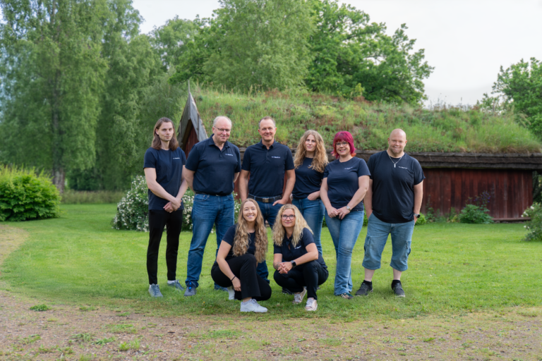 En gruppbild på ett några personer med träd och gammalt hus i bakgrunden. Det är gräs runt omkring. Personerna har en mörkblå t-shirt där det står fastbit.